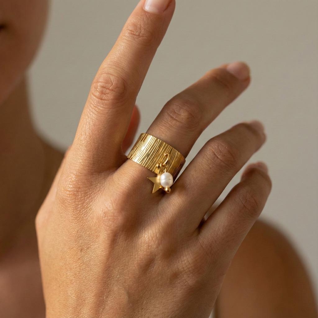 Bague Romy. Anneau large doré au motif texturé effet bois, breloques pendantes. Une perle blanche nacrée et une étoile dorée