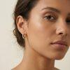Boucles d’oreilles créoles Huggie « Sophia » en acier inoxydable doré. Ornées de zircons étincelants sertis sur le devant